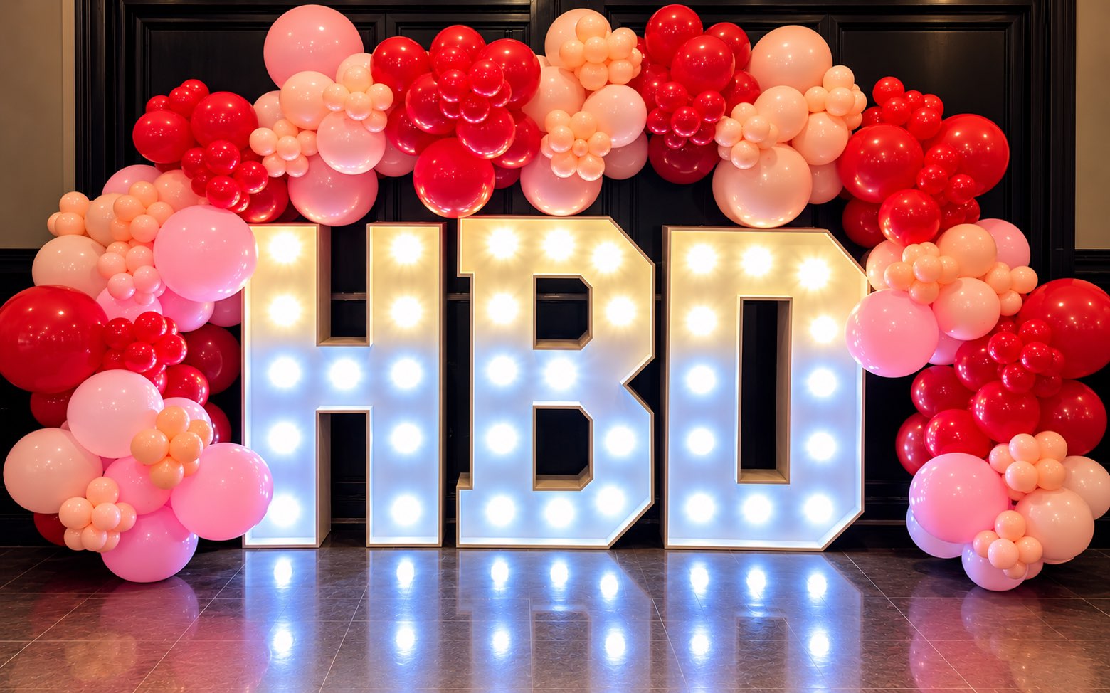 Illuminated HBD letters with a red, peach and pink balloon arch
