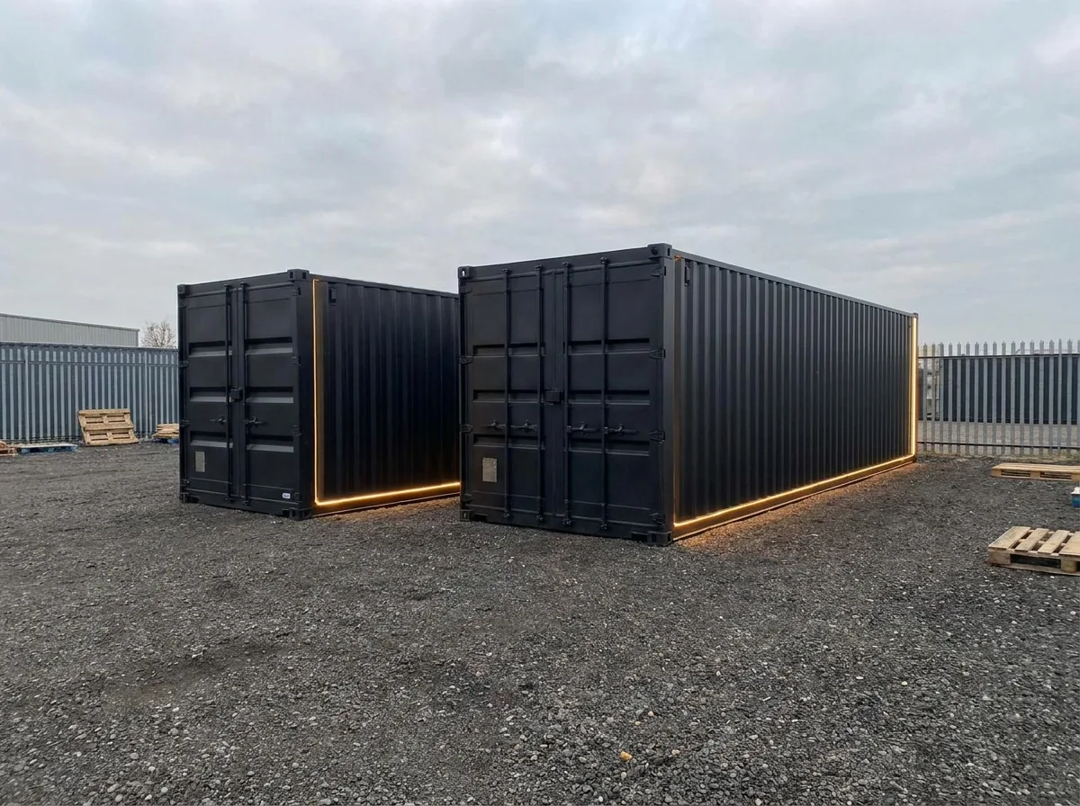 Two black shipping containers in different sizes in a clean yard